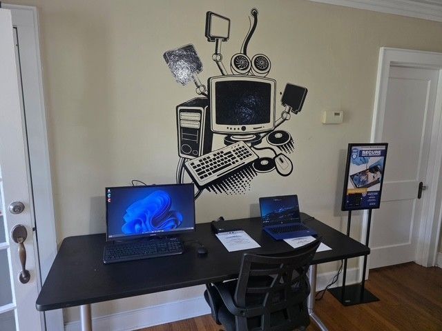 Home office with two laptops on a black desk and computer wall art above it