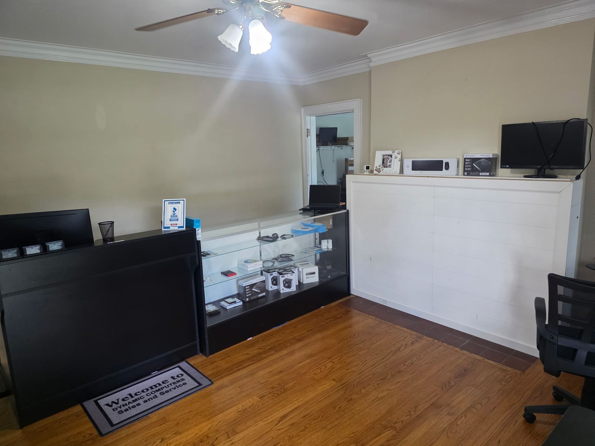Bright living room with wood floors, ceiling fan, TV, black sofa, and glass display cabinet