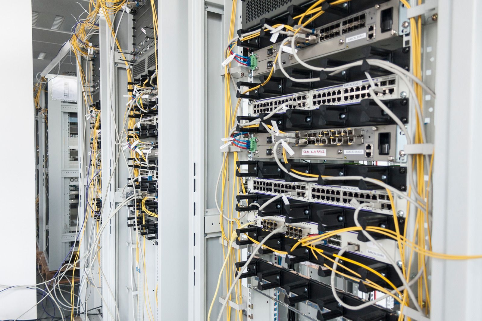 Rows of network servers and tangled yellow cables in a data center rack room