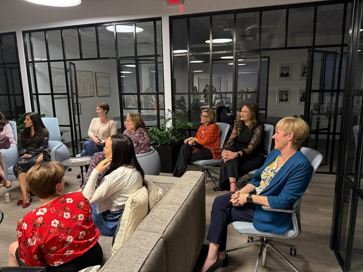 People seated in a glass-walled meeting room, listening attentively in a discussion.
