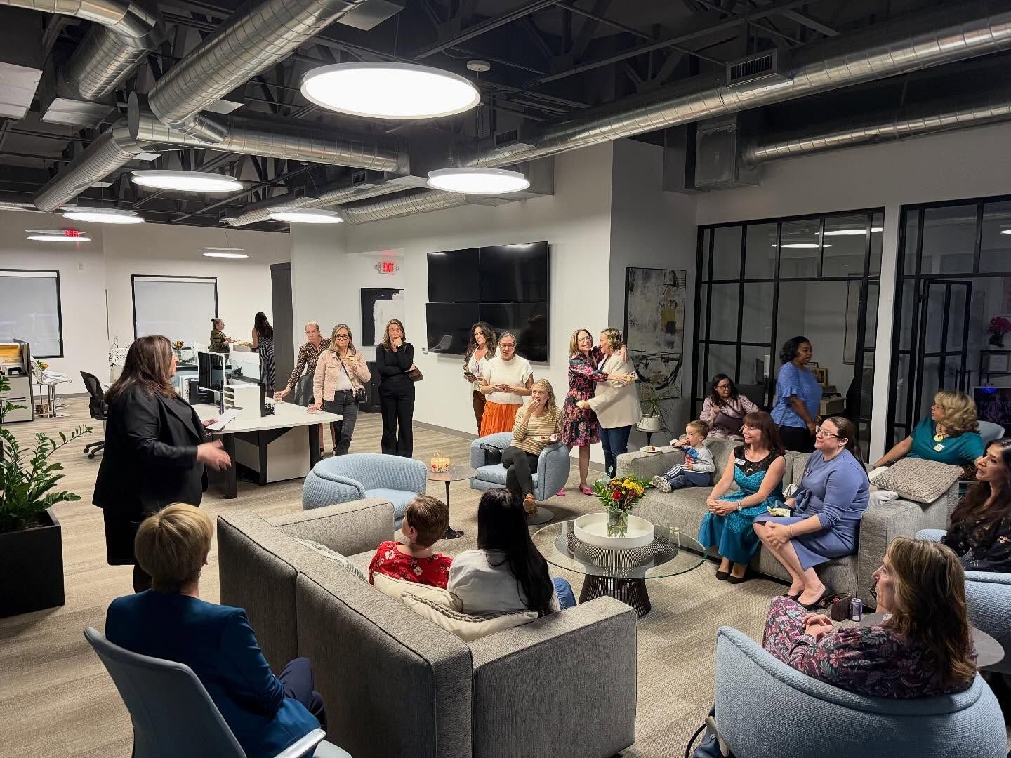 People seated in a modern lounge, listening to a presenter during a group discussion.