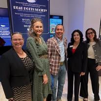 Five people posing indoors at an event booth, smiling in front of a blue promotional display.