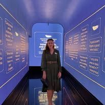 Woman standing in a blue-lit exhibition hallway with text panels on both walls