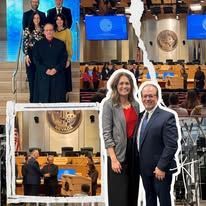 Two people posing in a large conference chamber with blue screens and a seal behind them.