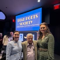 Three people posing in front of a Dead Poets Society poster in a dim theater lobby