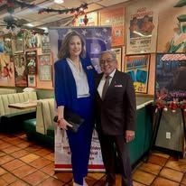 Two people posing in a diner, with retro decor and red booths in the background.