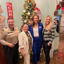 Four people pose indoors by a decorated Christmas tree and holiday wreaths.