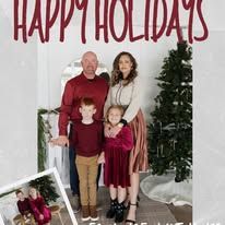 Family of four posing in front of a “Happy Holidays” backdrop with a Christmas tree and wrapped gifts.