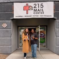 Two people standing outside 215 Mail Center storefront, smiling and posing together