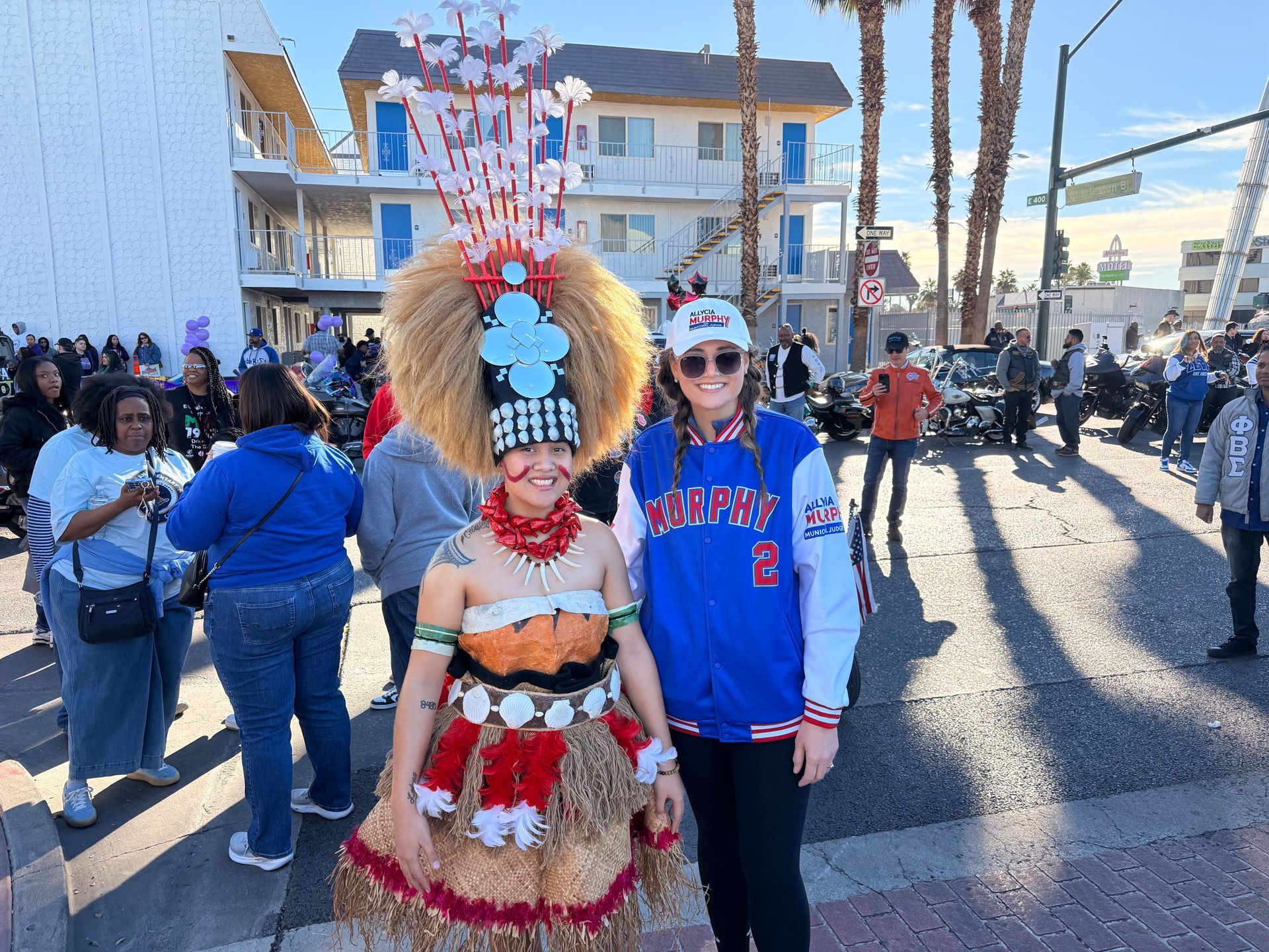 Two people in colorful costumes pose outdoors at a festive street event.