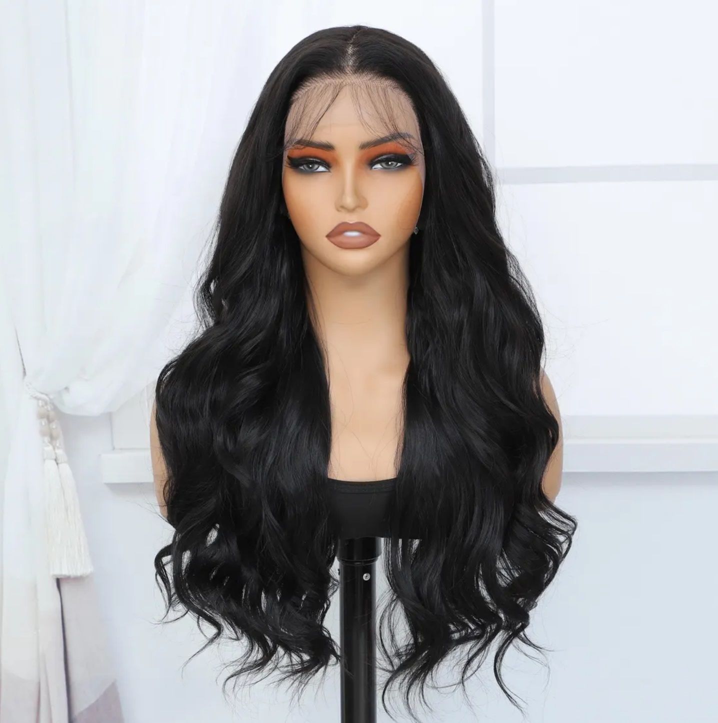 Black-haired mannequin wearing a wavy wig, posed indoors, with neutral facial expression and light makeup.