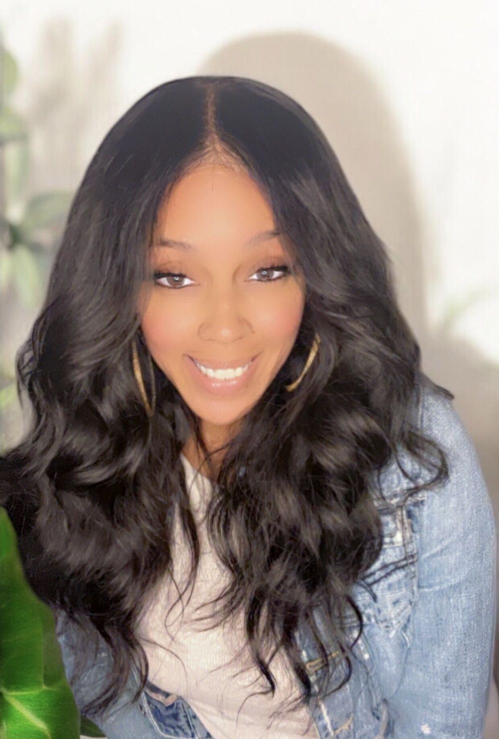 A woman wearing a wig and a denim jacket is smiling.