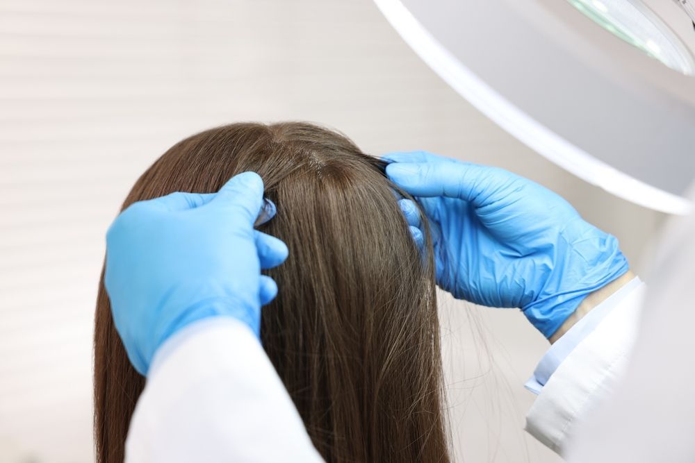 A doctor is examining a woman 's hair under a light.
