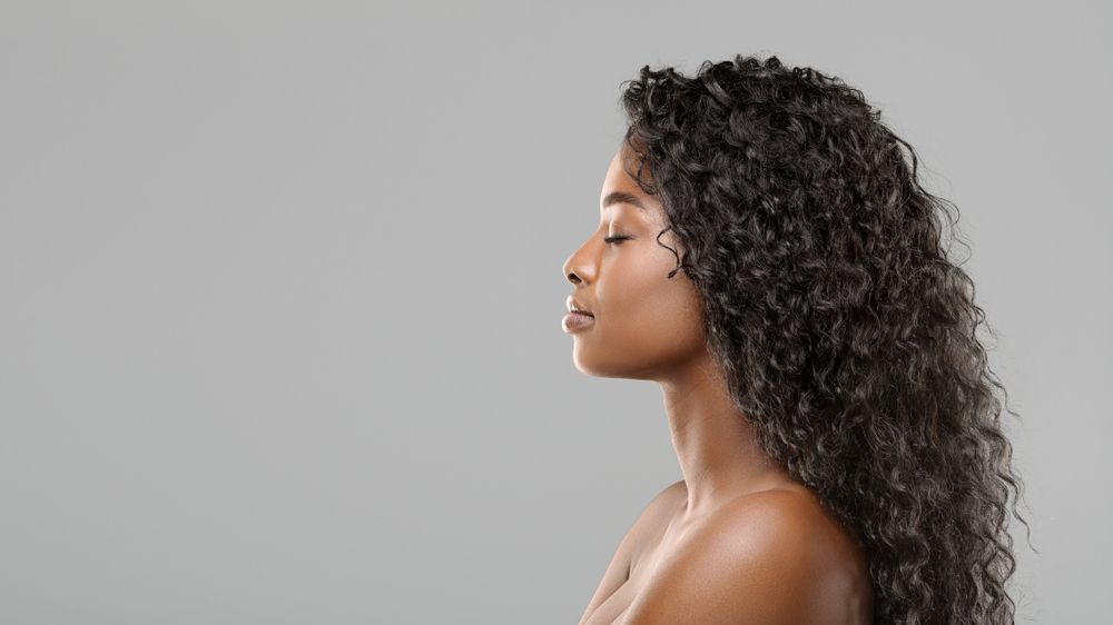 A woman with long curly hair is standing in front of a gray background.