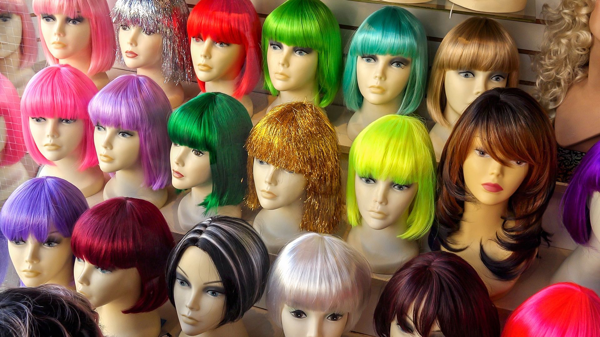 A bunch of mannequin heads with different colored wigs on them.