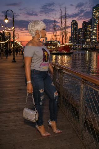 Side-profile portrait of a person with short platinum hair and large hoop earrings against a blurred city lights background