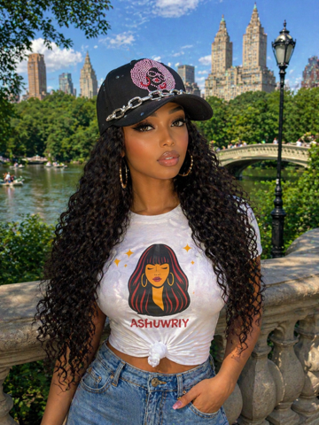 Woman posing by a park railing with city skyline and bridge in the background, wearing a black cap and graphic T-shirt