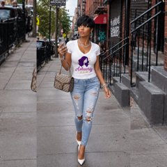 Woman in a white graphic T-shirt and ripped jeans sitting at a bar with a cocktail, warm lights behind her
