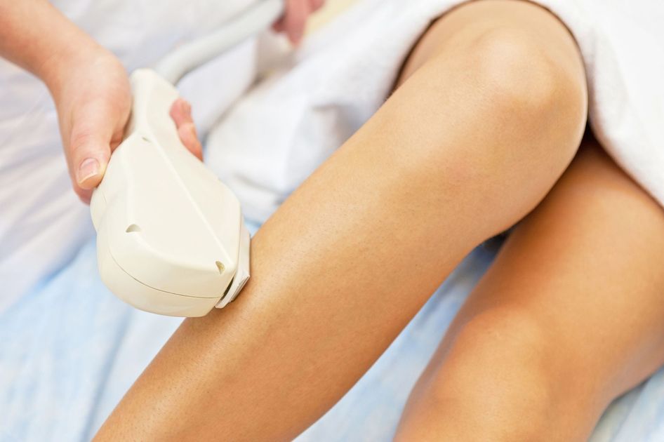 Un professionista appoggia un dispositivo laser per la depilazione sulla parte inferiore della gamba di una persona in un ambiente clinico.