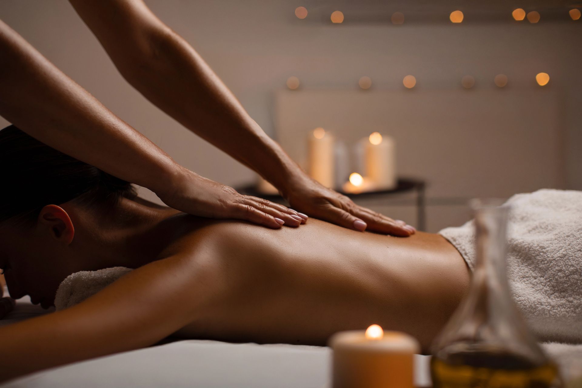 Una persona riceve un massaggio alla schiena in un ambiente intimo e illuminato da candele, tipico di una spa.
