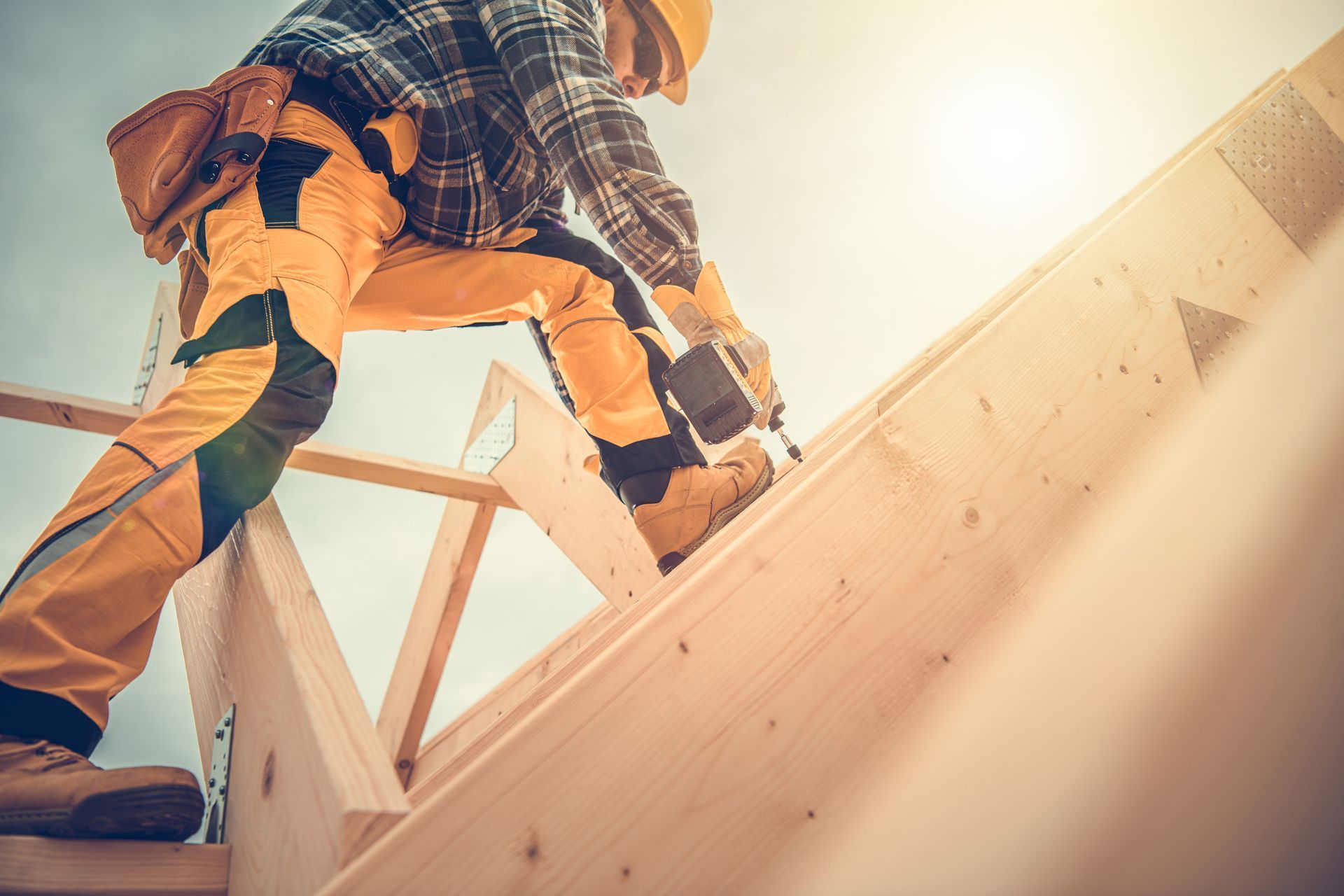 Commercial roofing contractor installing wooden roof framing with nail gun on sunny job site. Commercial roofing contractor installing wooden roof framing with nail gun on sunny job site.