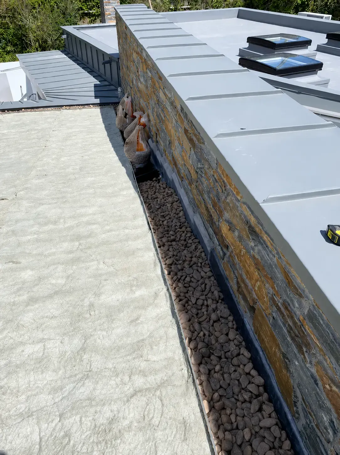 Flat roof system with metal cappings, rooflights and stone wall detailing