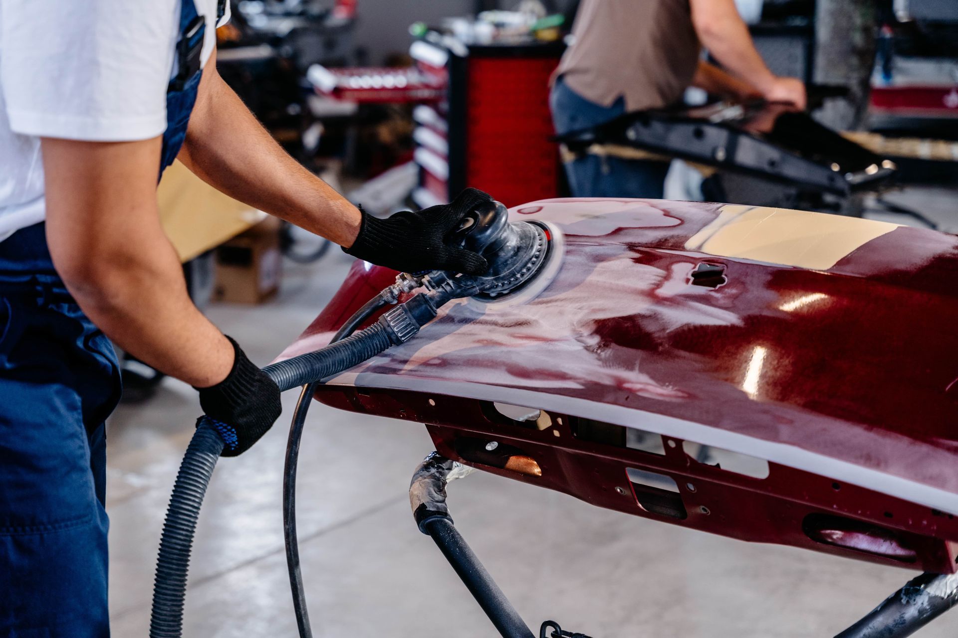 Worker sanding a red car hood in an auto body shop