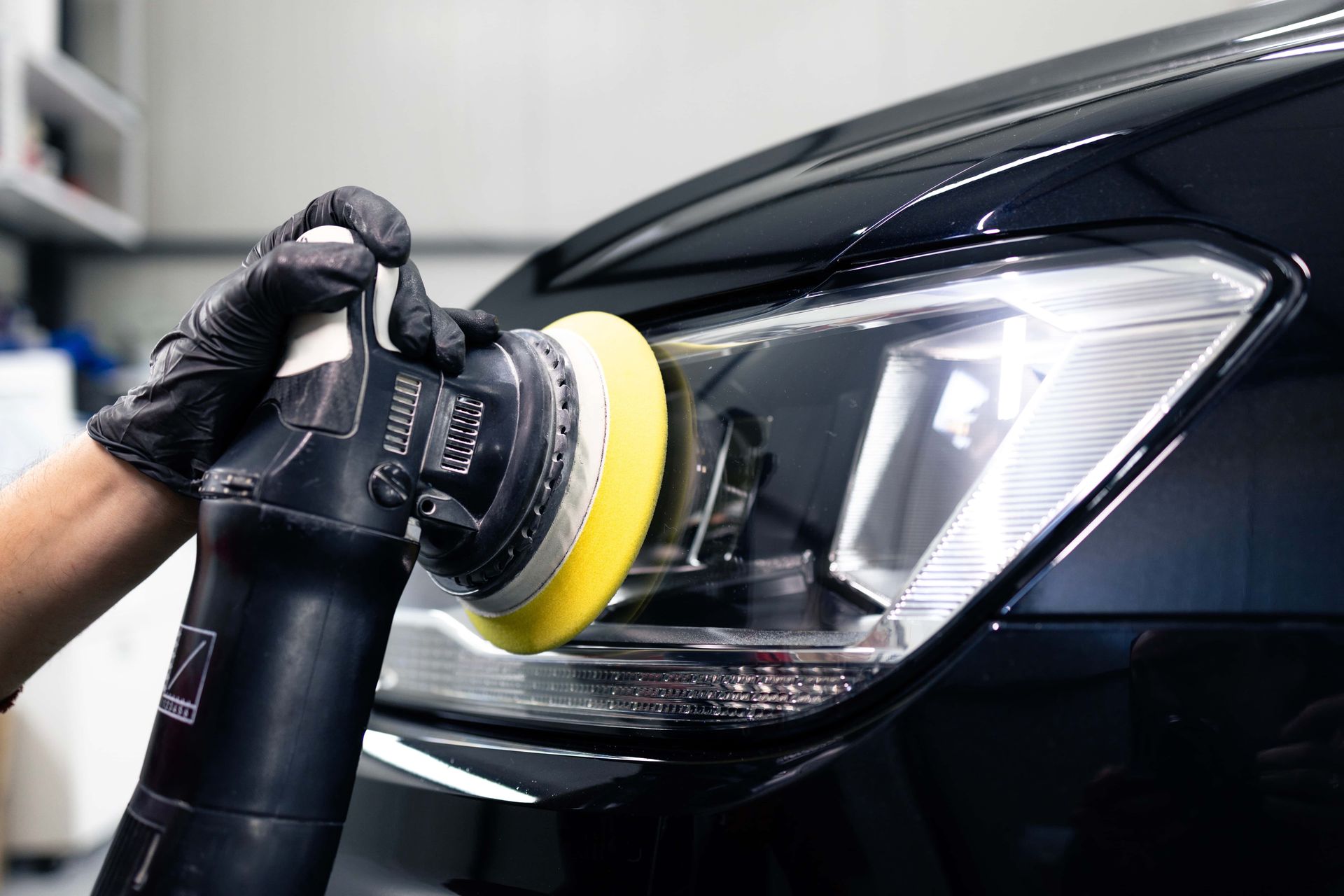 Hand polishing a black car headlight with a rotary buffer and yellow pad