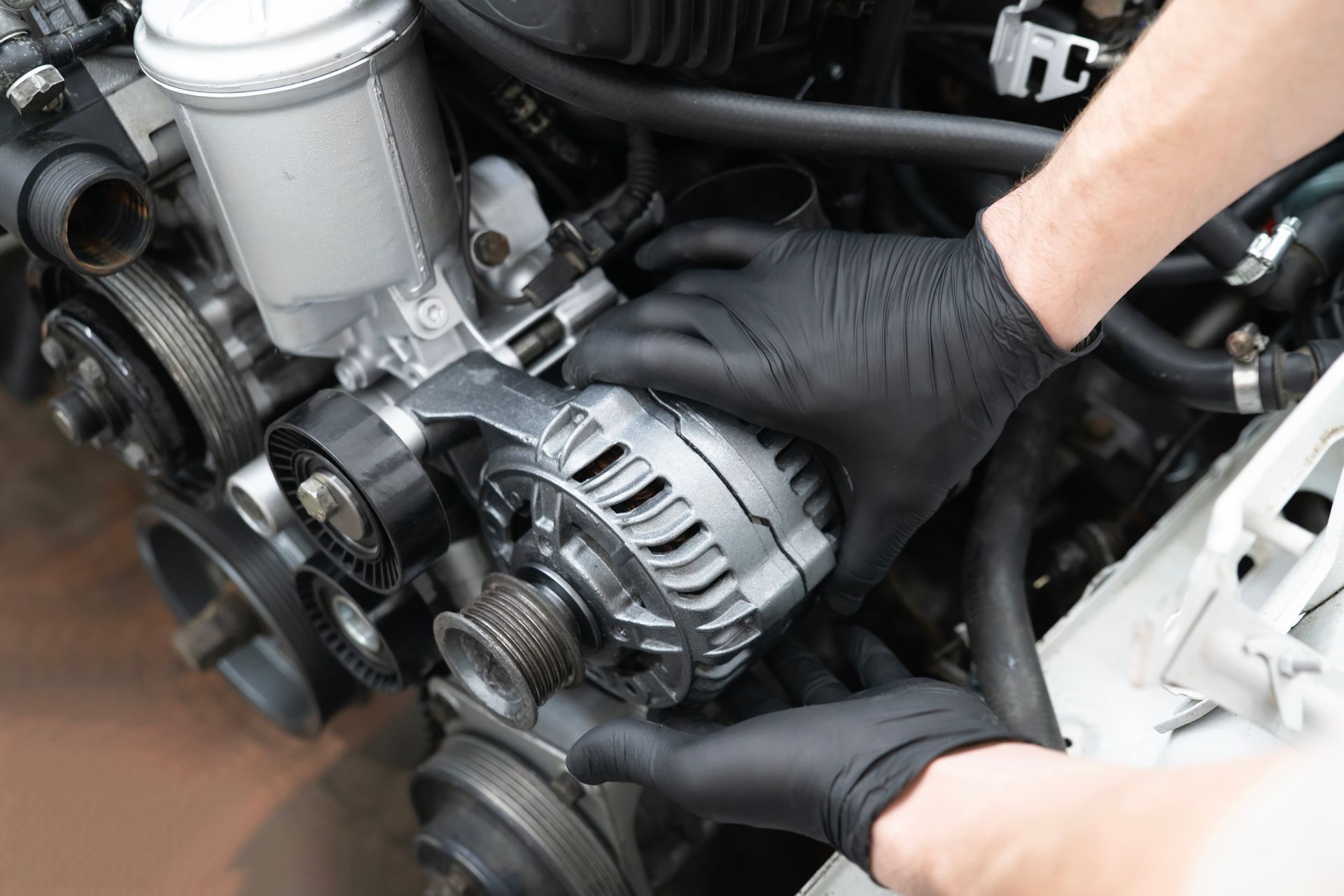 Gloved hands installing an alternator on a car engine with the serpentine belt removed