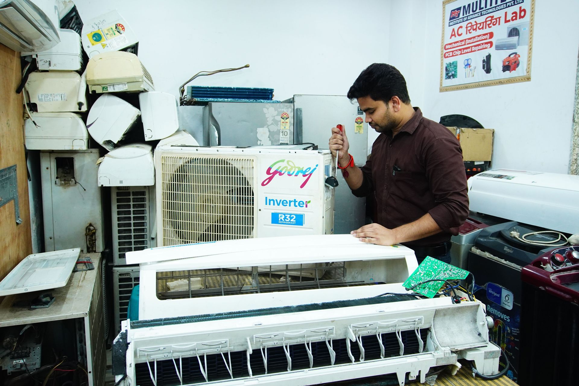 Man servicing a wall-mounted air conditioner in a workshop, with tools and equipment nearby