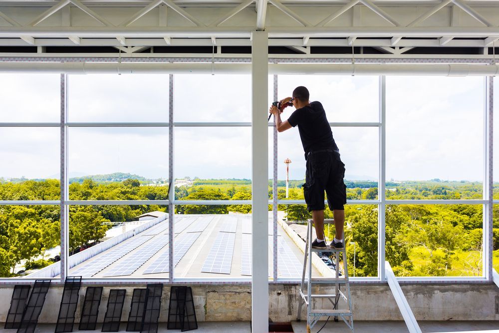 A man is standing on a ladder in front of a large window — Ideal Glass In Winnellie, NT