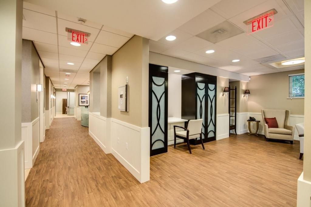 A long hallway with wooden floors and a red exit sign.