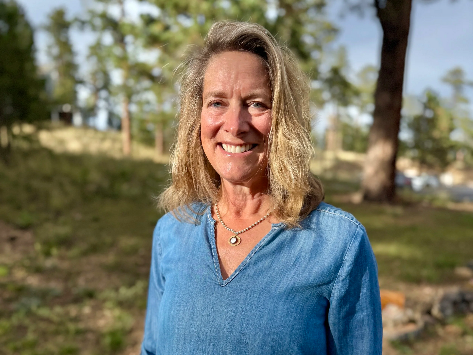 Woman with blonde hair smiling outdoors, wearing a blue shirt.