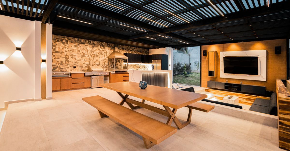 Salón moderno de planta abierta con mesa larga de madera, bancos, pared de piedra y televisor montado en la pared.