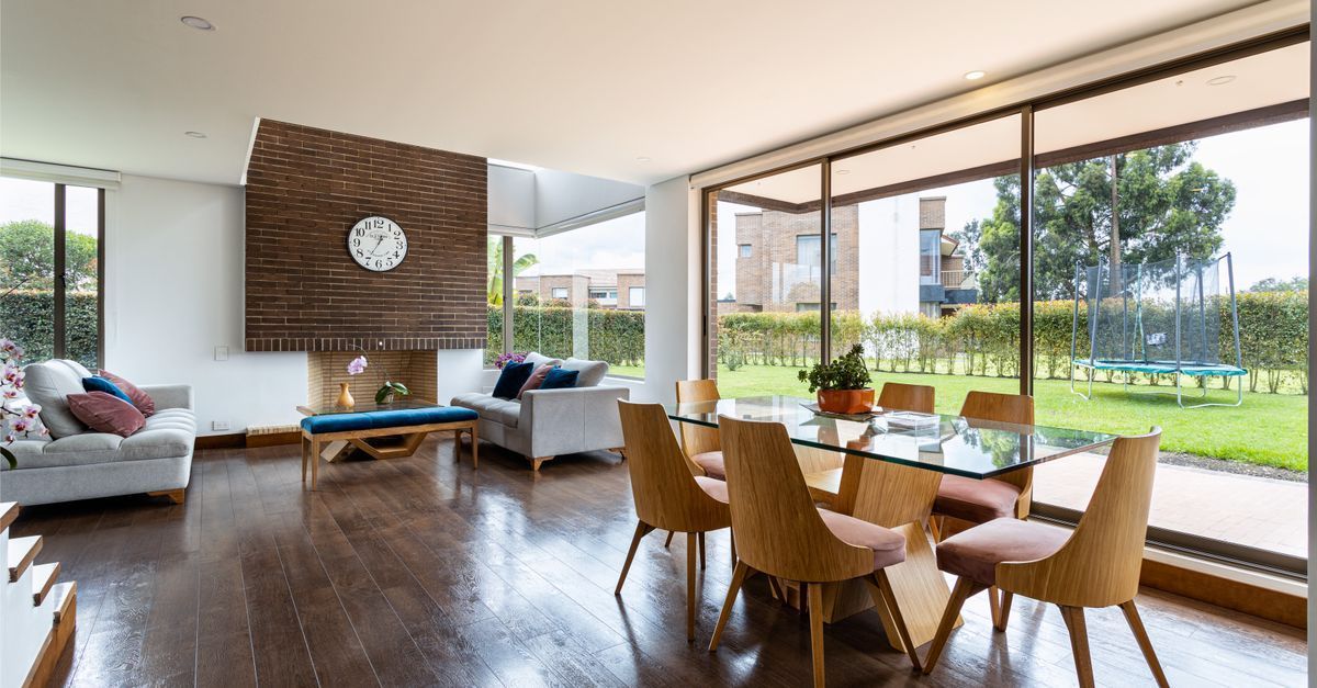 Luminoso salón con chimenea, mesa de comedor y grandes puertas de cristal que dan a un patio ajardinado.