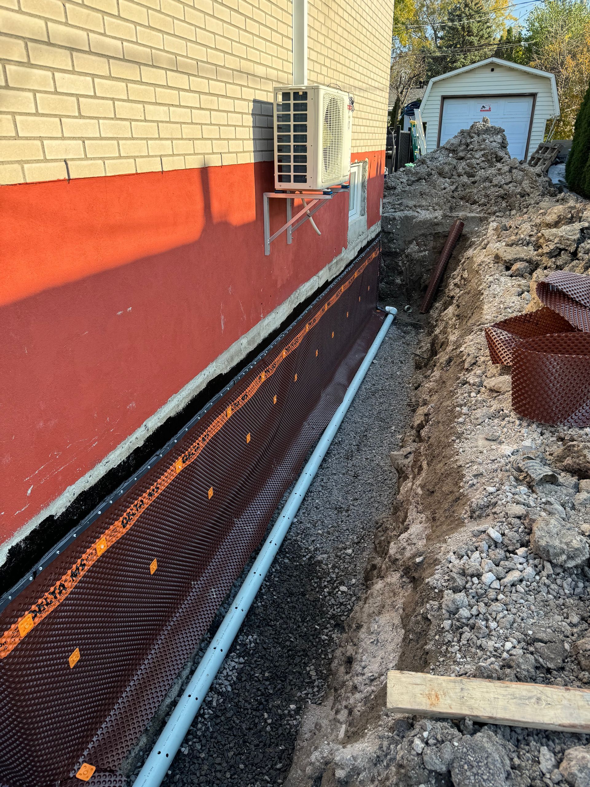 Un système de drainage est en cours d'installation sur le côté d'un bâtiment en briques.