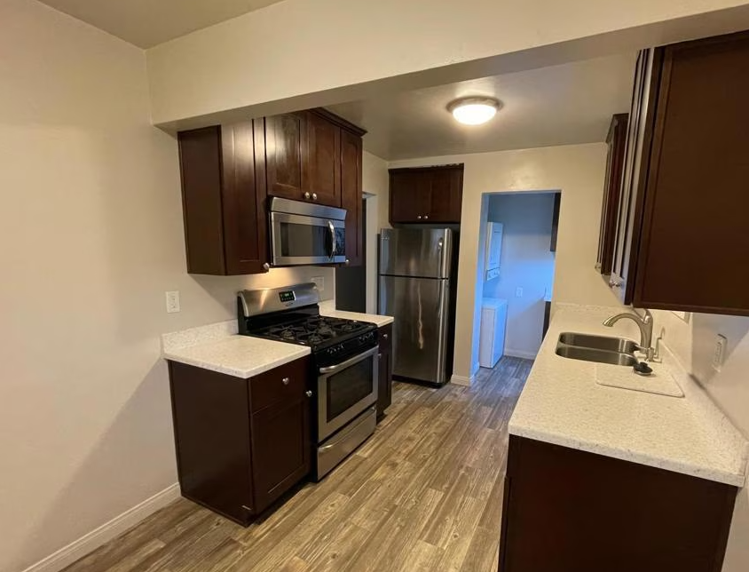 A kitchen with a stove , refrigerator , microwave and sink.