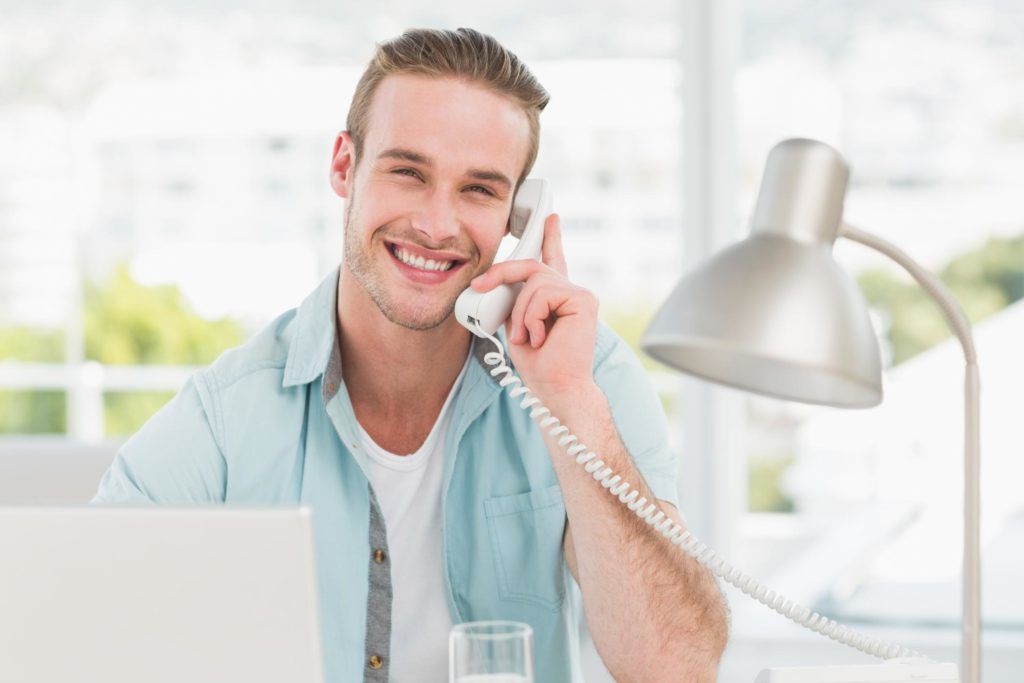 A man is sitting at a desk talking on a telephone.