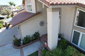 An elevated view of a house entrance with a tan stucco exterior, tile roof, brick-lined landscaping, and a large pillar.