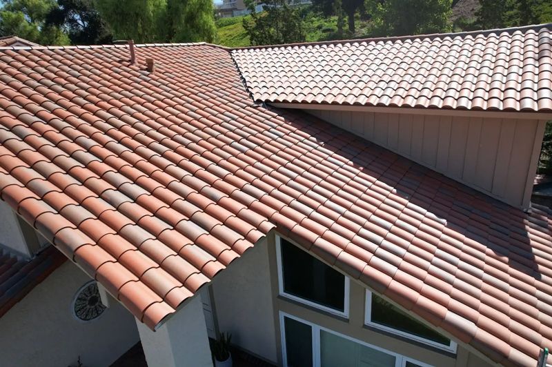 High-angle view of a residential roof featuring terracotta-colored clay tiles, a beige exterior wall, and window sections.