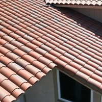 A high-angle view of a residential roof covered in textured, reddish-brown terracotta tiles over a beige exterior wall.
