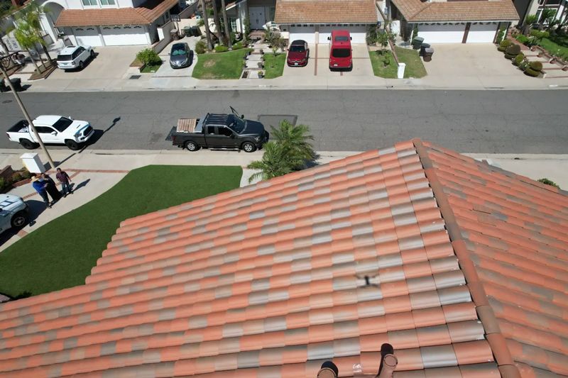 Aerial view of a brown tiled roof with a residential street, parked cars, and pedestrians below.