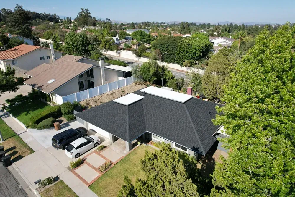 Aerial view of a residential house with a new dark shingled roof, white trim, and two cars parked in the driveway.