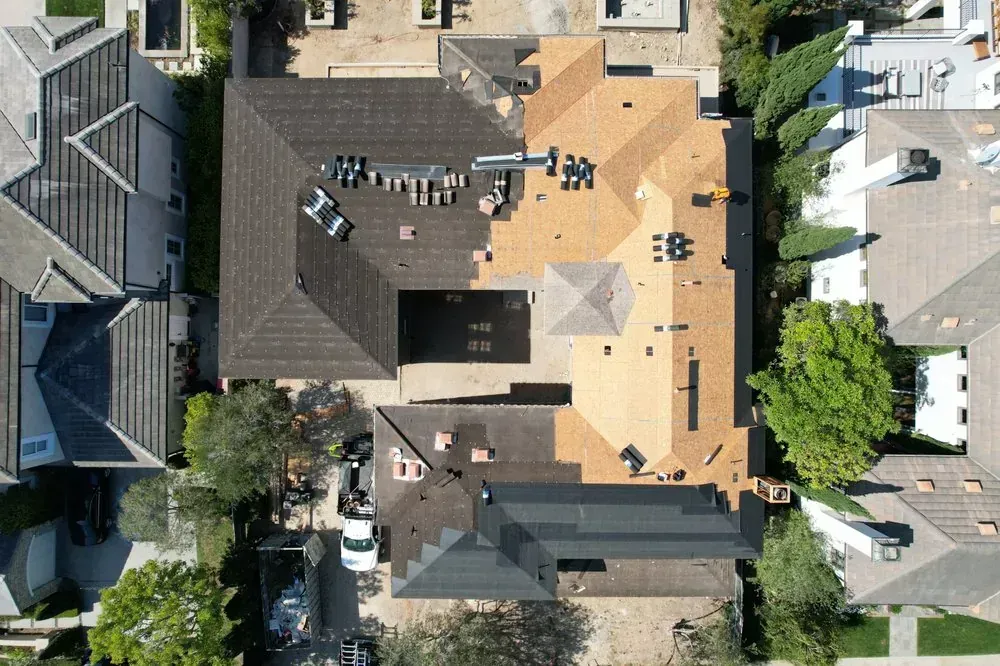 Top-down drone view of a house roof undergoing a mid-project replacement with a mix of old dark and new tan shingles.