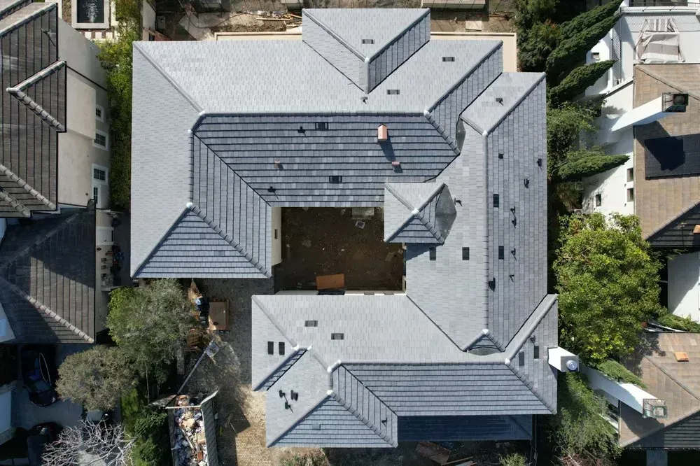Aerial view of a large residential gray tile roof with an open courtyard in the center, surrounded by neighboring homes.