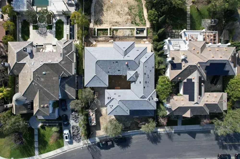 A high-angle aerial view of three residential homes with grey roofs, separated by narrow driveways and trees.