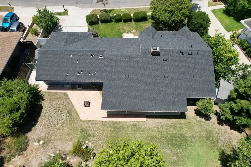 Aerial view of a dark shingled roof on a residential home with a patio and surrounding yard.