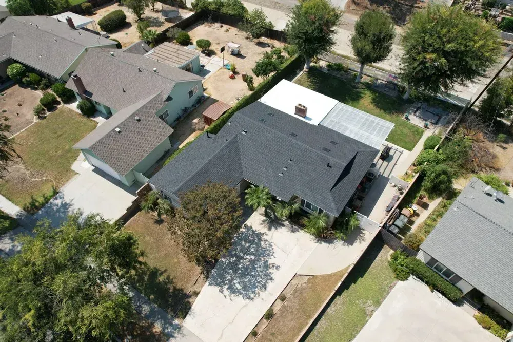 An aerial view of a residential neighborhood with several houses, paved driveways, and trees on a sunny day.