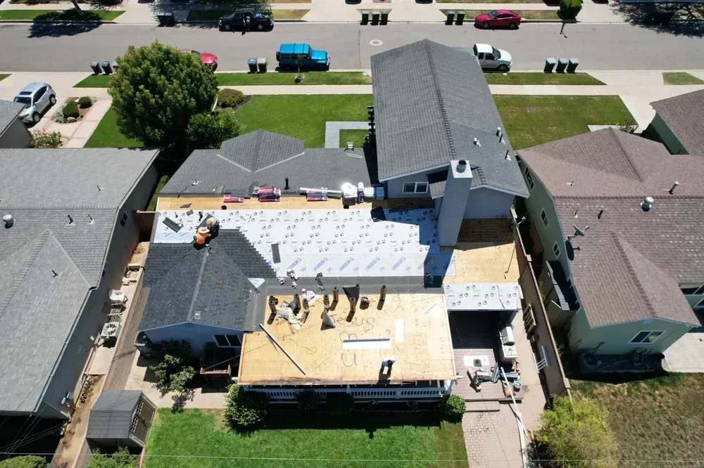 Aerial view of a residential roof replacement in progress with workers visible on sections of exposed plywood decking.