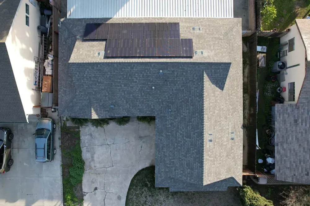 An aerial view of a gray shingled roof with a dark solar panel array installed on the upper section.
